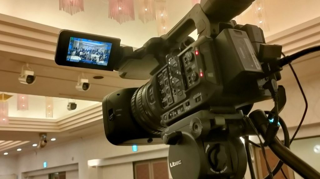 Libec三脚にセットされたCanon XF605業務用ビデオカメラ。モニター画面に会場全景を表示