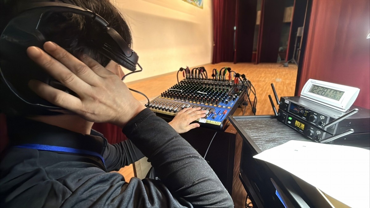 屋内会場のステージ前で、ヘッドホンを装着しミキサー卓を操作する音響スタッフの様子。滋賀県東近江市の能登川ふれあいフェスタにて。