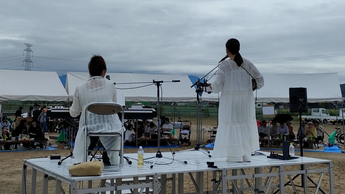 滋賀県東近江市の自治会のお祭りで、屋外ステージにてキーボード演奏とボーカルのパフォーマンスを行う演者と音響の様子。瓜生津町ふれあい祭りにて。