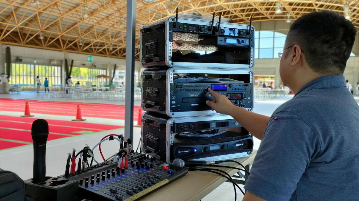 室内会場の企業イベントにて、音響機材ラックやミキサーを調整するPAオペレーターの様子。滋賀県愛荘町ラポール秦荘はつらつドームで開催された「だいかねまつり(主催:株式会社大兼)」